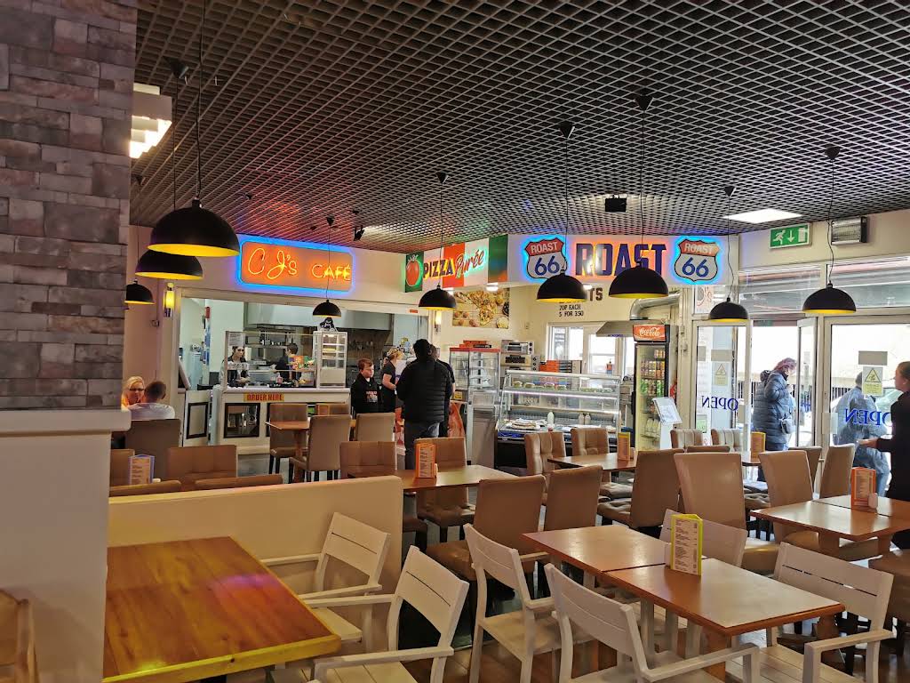 CJ’s Café Bistro dining room with wooden tables, cream chairs, pendant lights and an orange CJ’s Café sign